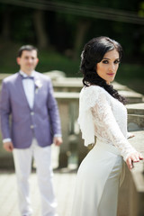 Beautiful bride posing on old balcony, groom in background