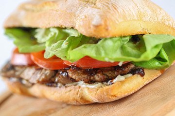 Tasty pork steak sandwich in a ciabatta with tomatos, lettuce, mayonnaise and barbecue sauce