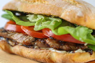 Tasty pork steak sandwich in a ciabatta with tomatos, lettuce, mayonnaise and barbecue sauce
