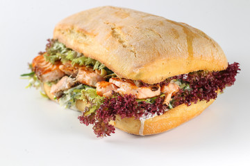 Tasty salmon steak sandwich in a ciabatta with lettuce, scallion sauce, capers, dill and basil