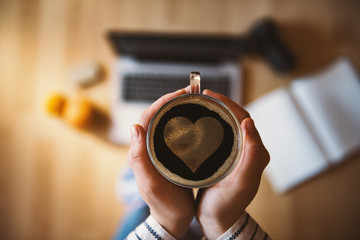 Girl holding a cup of coffee with heart symbol.