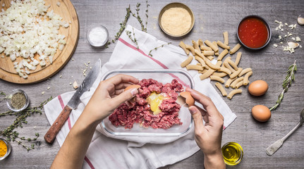 female hands, mix ground beef, penne pasta, eggs, breadcrumbs on wooden rustic background top view close up