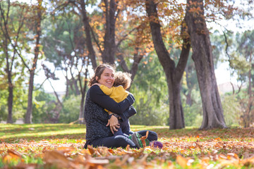 Naklejka na ściany i meble colorful autumn scene. Hug of mom and baby sitting in the park