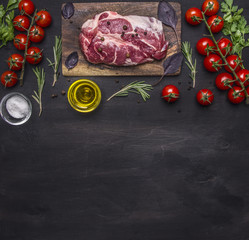 raw pork steak for the grill, on a cutting board with vegetables and herbs, rosemary border ,place for text  on wooden rustic background top view close up