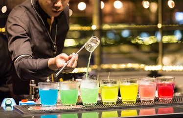 A group of shot glasses with a rainbow of colored drinks.