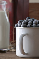 Photo of a frozen blueberrys in metal mug and bottle of milk standing on old wooden table.