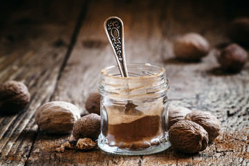 Ground nutmeg in a jar and whole nuts on an old wooden backgroun - obrazy, fototapety, plakaty