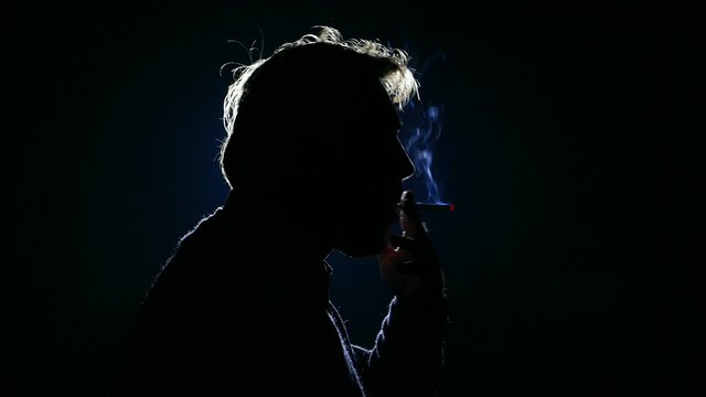 male man lights a cigarette and smokes a cigarette, silhouette of person in smoke