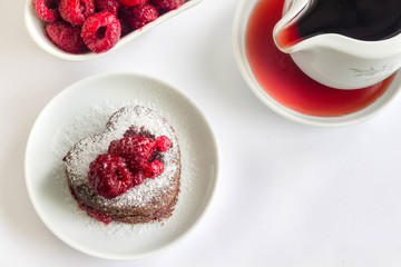 Heart-shaped chocolate cake with fresh fruit on top, top view, white background.