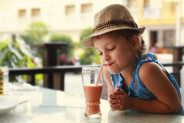 Cute thinking kid girl drinking tasty juice in street restaurant