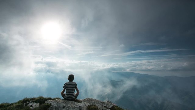 Men meditating over mountain between clouds
