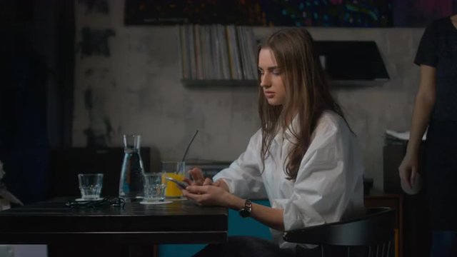 Young attractive Caucasian female using her phone in retro styled cafe. 4K cinemagraph - motion photo seamless loop