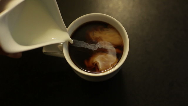 A cup of hot coffee with milk on the black table in slow motion