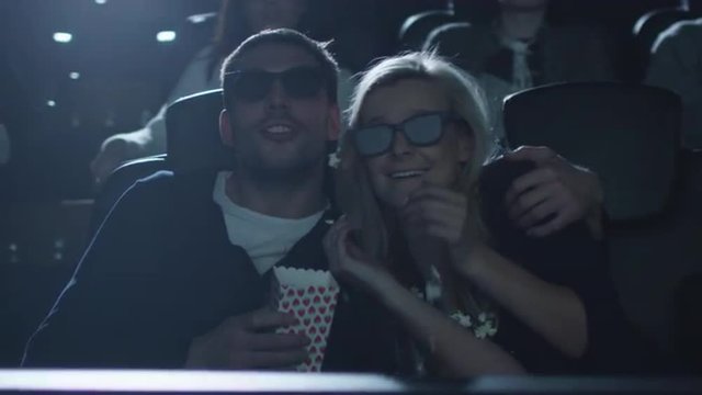 Couple embrace each other while popcorn is shaken out of the box during a fun 5d film screening in cinema.  Shot on RED Cinema Camera.