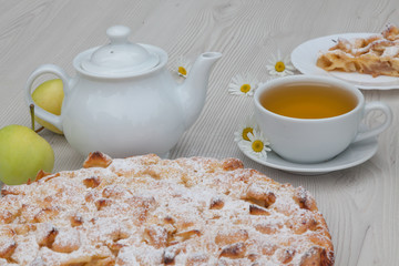 Apple pie and camomile tea set on the white wooden table decorated with fresh flowers and apples.