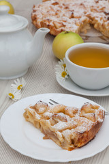 Apple pie and camomile tea set on the white wooden table decorated with fresh flowers and apples.