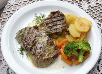Grilled beef steaks on a plate with potatoes, baby carrots and broccoli