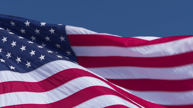A United States flag blows in the wind against a blue sky. Shot in slow motion 4K UHD.