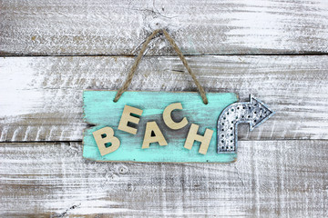 Beach sign with directional arrow hanging on rustic background