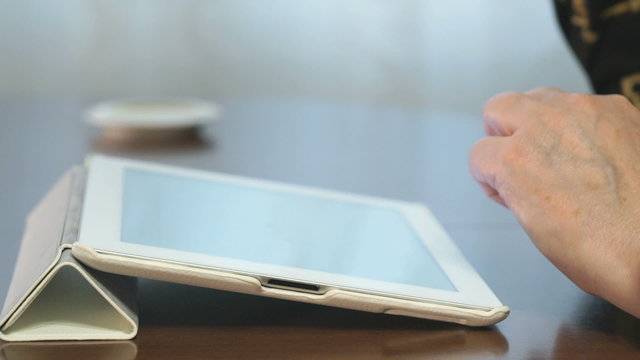 Woman works over documents using a digital tablet and drinks coffee