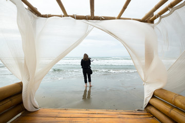 femme de dos au bord de la mer au premier plan les voiles blanches d'un lit de plage