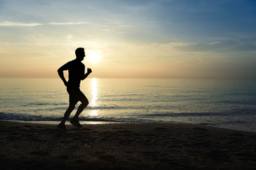 Fototapeta na wymiar silhouette young sport man running outdoors on beach at sunset with orange sky