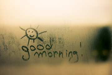 Happy sunny face sign with good morning written on foggy window background. 