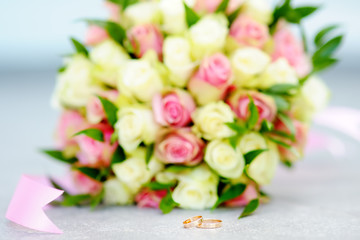 Two gold wedding rings with beautiful wedding flowers bouquet with on background
