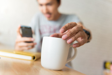 young man drinking coffee in cafe and looking at the phone screen