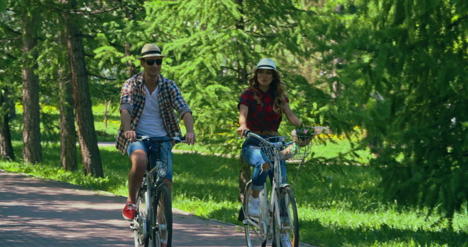 Young Asian couple on bicycles riding through green park on warm summer day and talking