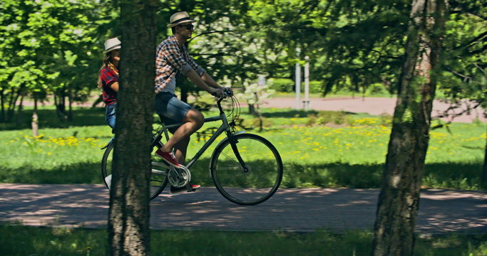 Tracking shot of man giving his girlfriend a ride on his bicycle in green park 