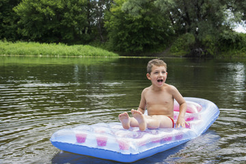 Summer on the river boy sits on an inflatable mattress on the ri
