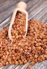 Heap of buckwheat groats with spoon on wooden surface