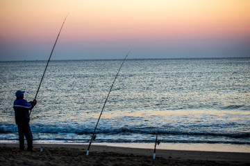 Angler im pastellfarbenen Sonnenaufgang am Meer