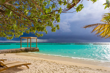 Pavilion at white sand beach in front of storm at Maldives
