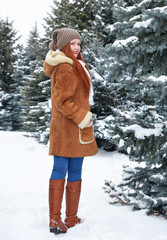 Girl walk in winter park at day. Fir trees with snow. Redhead woman full length.