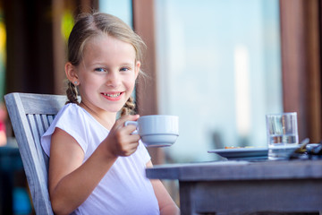 Adorable little girl having breakfast with hot cacao at cafe