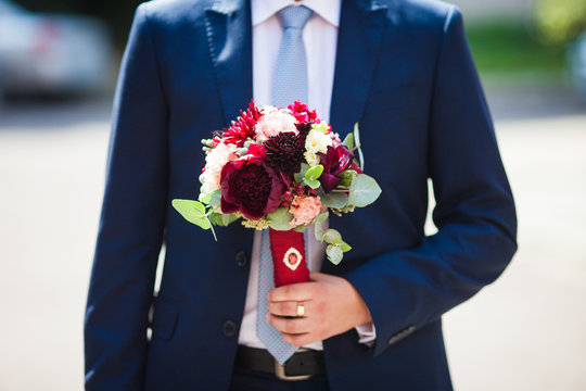 Elegant handsome groom in blue suit with wedding bouquet
