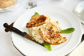 Pork medallions with barley risotto on white plate, knife and herb
