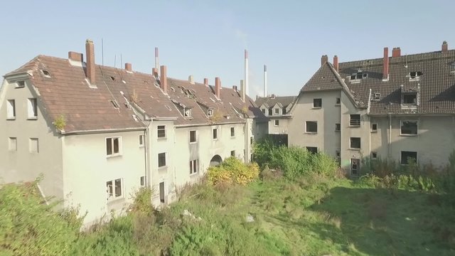 Aerial of an abandoned quarter in the coal-mining town Gladbeck, Germany,
slow ascent forward over meadow and shabby houses ending on a working power plant, recorded with flat s-log colour profile.