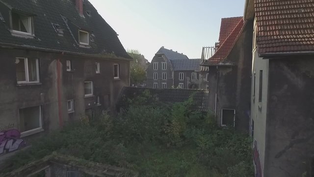 Aerial of an abandoned quarter in the coal-mining town Gladbeck, Germany, low altitude flight, medium tracking shot forward between shabby overgrown houses. recorded in flat s-log colour profile.
