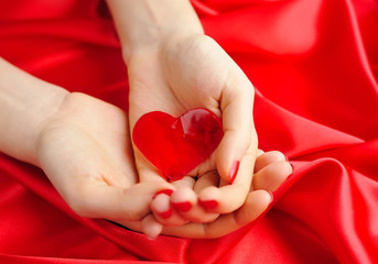Obraz na płótnie Canvas Heart candy in women's hands against a background of red silk