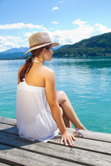 Junge Frau sitzt im Sommer am See auf dem Bootssteg. W&ouml;rthersee. K&auml;rnten. &Ouml;sterreich