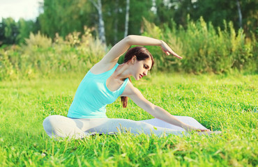 Young woman doing yoga exercises on grass in summer day