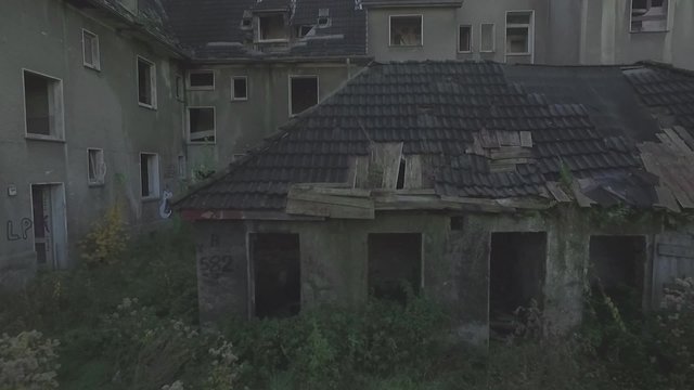 Aerial of an abandoned quarter in the coal-mining town  Gladbeck, Germany, low altitude, close tracking shot with slow ascent forward over shabby house top and chimney, panning. flat s-log.