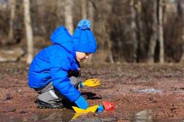 little boy plaing with paper boats in spring puddle