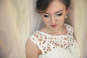 Beautiful bride in vintage white dress posing under curtain