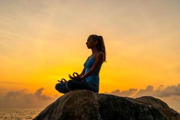 Woman sitting on a rock near sea and meditate at dawn on a tropical island Koh Samui, Thailand