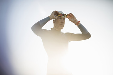 A swimmer in a wetsuit and swimming hat, adjusting his swimming goggles. 