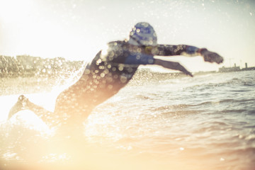 A swimmer in a wet suit running into the water, making a splash. 